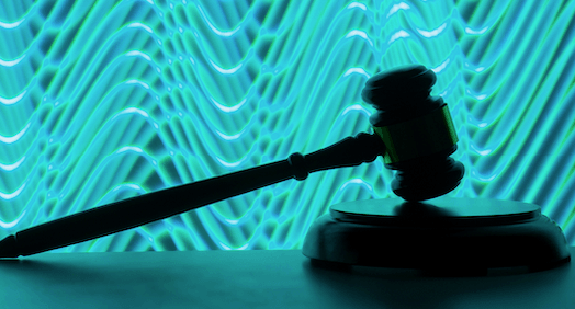 A brown silhouetted gavel leans on a block against a backdrop of swirling blue lines.