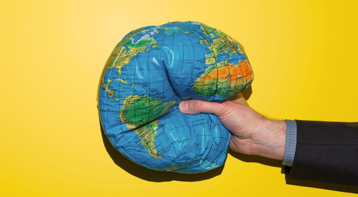 Hand holding blue and green globe on bright yellow background