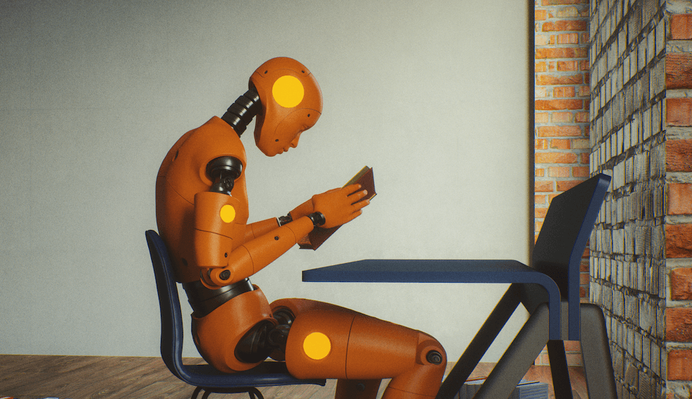 An orange crash-test dummy sits at a desk reading a book.